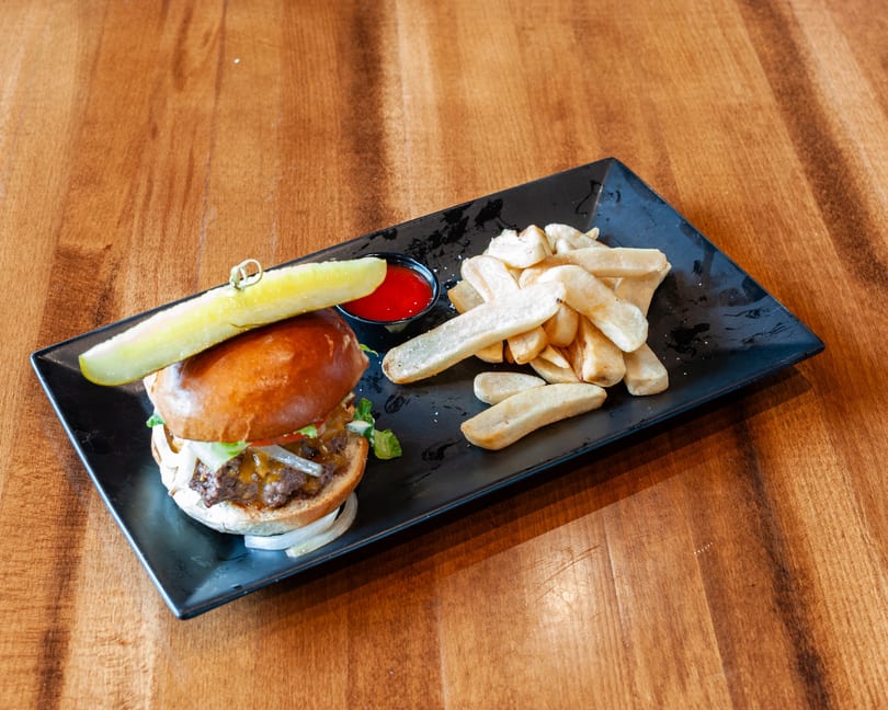 A cheeseburger with lettuce, tomato, onion, and a pickle spear, served with fries and ketchup on a black plate.