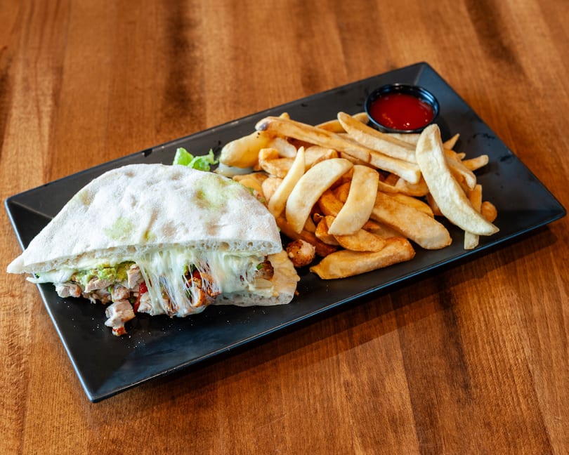 A chicken quesadilla with melted cheese and guacamole, served with golden french fries and ketchup.